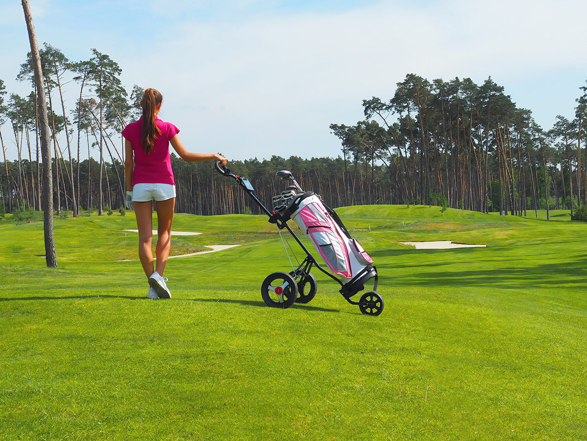 Female golfer on a golf course with a golf cart.